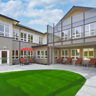 A modern building with a courtyard featuring a green lawn and an outdoor seating area.