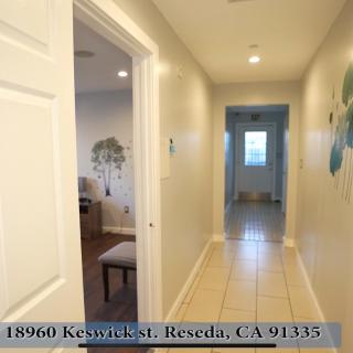 A view of a brightly lit hallway in a home, featuring clean walls and tiled flooring.