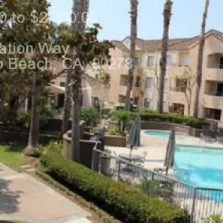 View of an apartment complex with a swimming pool and palm trees.