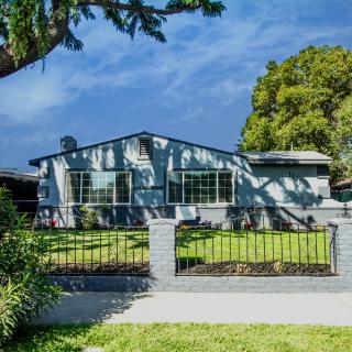 A suburban house with a spacious yard and a metal fence under a clear blue sky.