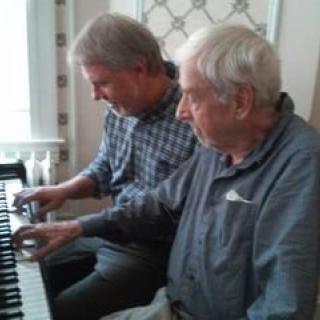 Two men playing a duet on the piano indoors.