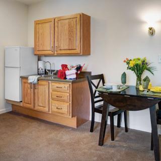 A cozy apartment kitchen and dining area with wooden cabinets, a small fridge, and a table set for two.