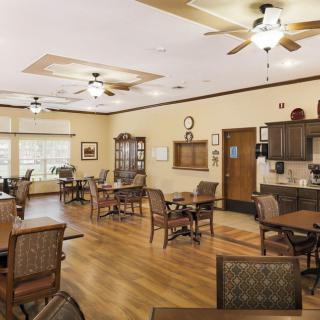 A spacious dining area with wooden flooring, tables, chairs, ceiling fans, and a kitchenette.