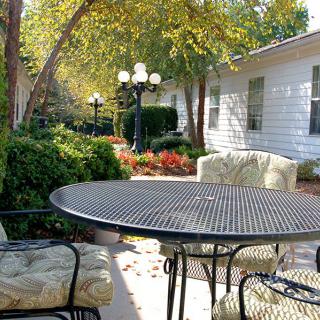 A cozy outdoor patio with a round table, cushioned chairs, and lush greenery.