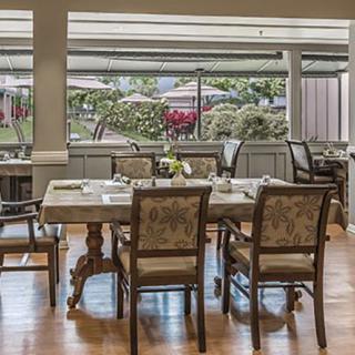A cozy restaurant dining area with elegantly set tables and chairs, overlooking a garden through large windows.