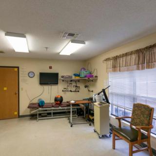 A rehabilitation therapy room equipped with medical apparatus, a window with curtains, and seating.