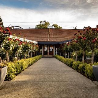 A picturesque pathway lined with lush rose bushes leading to a building under a cloudy sky.