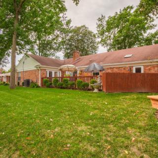 A suburban backyard with a lawn, trees, and outdoor seating area next to a brick house.