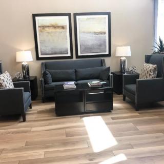 A modern living room featuring a dark sofa and chairs, wooden flooring, complemented by lamps and abstract artwork.