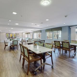 A spacious dining room with neatly arranged tables and chairs, featuring warm lighting and wooden flooring.