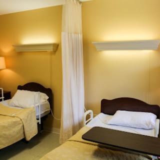 A well-lit hospital patient room featuring two beds separated by a curtain.