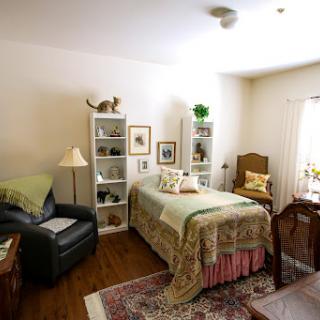 A cozy and well-decorated bedroom featuring a twin bed, bookshelves, and comfortable seating.
