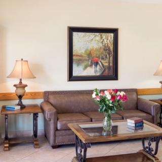 A cozy living room with a brown sofa, a coffee table with a vase of flowers, two side tables with lamps, and a painting on the wall.
