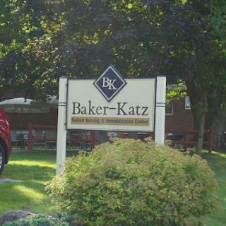 A sign for Baker-Katz displayed in a green outdoor setting.
