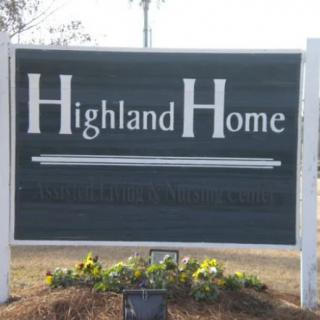 A sign displaying the name 'Highland Home' with some plants at its base.