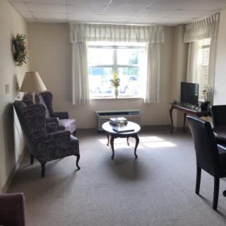 A cozy living room with a sofa, armchair, and coffee table, featuring neutral tones and a window allowing natural light.