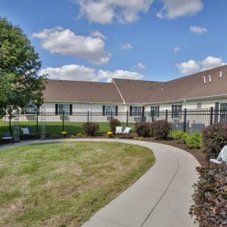 A scenic view of a building with a pathway surrounded by greenery and trees under a partly cloudy sky.