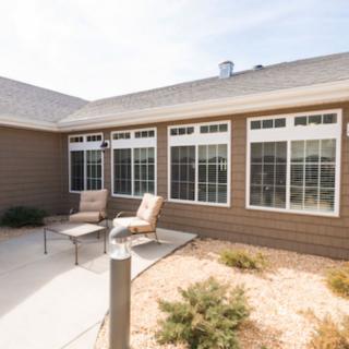 A sunny patio with comfortable chairs and large windows on the house exterior.