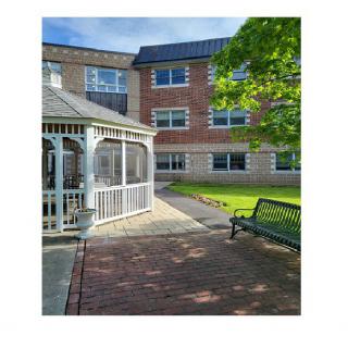 A scenic outdoor area with a gazebo and bench by a brick pathway next to a building.