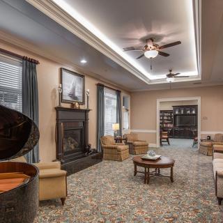 A cozy lounge area with a fireplace and piano, featuring comfortable seating and a ceiling fan.