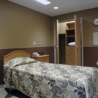 A simple hospital room with a bed, wardrobe, and telephone.