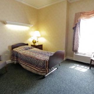 A cozy single bedroom with a carpeted floor and natural light coming through the window.
