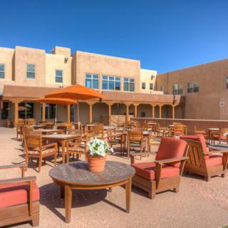 A sunny patio with wooden furniture and an umbrella, set against a building with desert-style architecture.