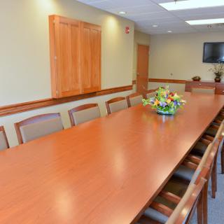 A spacious conference room featuring a long wooden table and a floral centerpiece, designed for meetings.