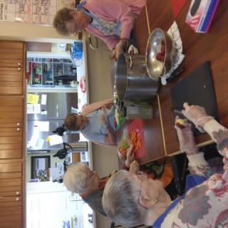 A group of elderly people preparing food together in a kitchen setting.