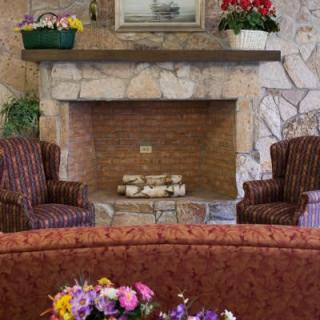 A cozy living room with a stone fireplace surrounded by two upholstered chairs and floral decorations.