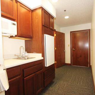 A compact kitchen area featuring wooden cabinets, a microwave, sink, and refrigerator.