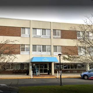 A three-story healthcare facility with a blue awning at the entrance.