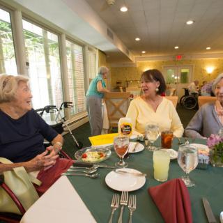 A group of elderly people enjoying a meal and conversation at a communal dining table.