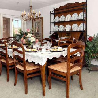 A traditional dining room with a large wooden table set for a meal, surrounded by matching chairs. A chandelier hangs overhead, and a china cabinet stands against the wall displaying dinnerware.