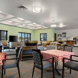 A spacious and well-lit dining area with tables and chairs, featuring a television and large windows.