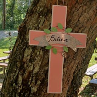 A beautifully painted cross hanging on a tree, promoting the message of 'Believe'.