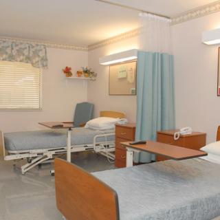 A well-lit and organized hospital patient room featuring two adjustable beds, a privacy curtain, and basic furniture.