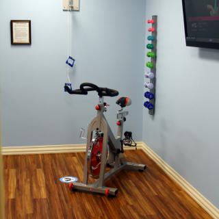 A small home gym setup with a stationary bike and a rack of weights against the wall.