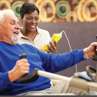 An elderly man enjoying a workout session with assistance from a supportive staff member.