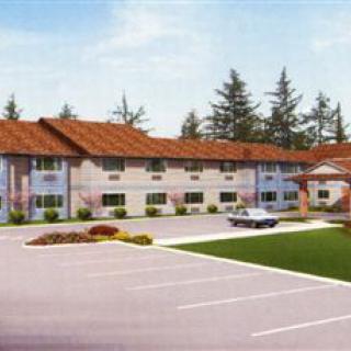 A two-story building with a parking lot in front, surrounded by trees.