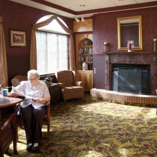 An elderly person reading in a cozy living room with a fireplace.