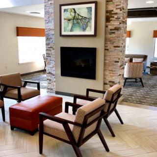 A modern seating area with a fireplace, featuring comfortable chairs and artwork in a well-lit space.