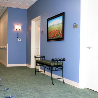 A hallway with blue walls, featuring a bench, artwork, and a light fixture.