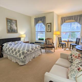 A cozy and well-lit bedroom featuring a comfortable bed, seating area, and natural light from the windows.