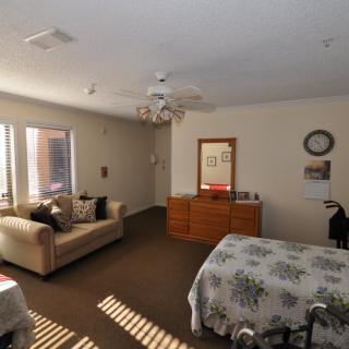 A cozy bedroom with a sofa, bed, dresser, and ceiling fan illuminated by natural light.