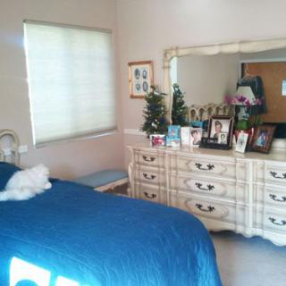 A cozy bedroom featuring a dresser with a mirror adorned with personal photos and decorative items, alongside a bed covered in a blue bedspread.