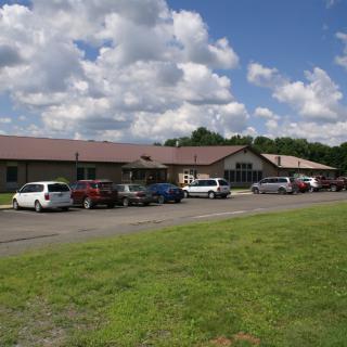 A rural building with a parking lot and several cars under a partly cloudy sky.