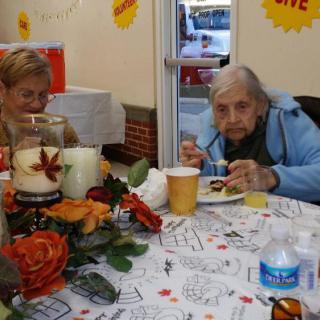 Two elderly individuals enjoying a meal at a decorated table with autumn-themed decorations.