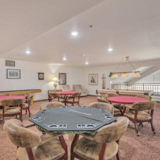 A spacious game room featuring multiple poker tables and comfortable seating under bright lighting.