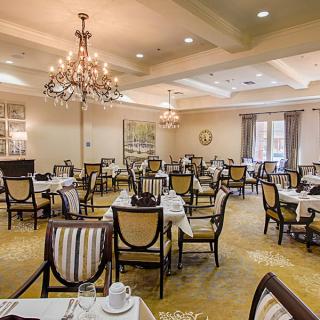 An elegant dining area with neatly arranged tables and chairs, accented by chandeliers.